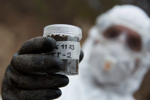 Un hombre con un traje de protección y guantes sujeta una muestra de tierra para analizar la radiación.