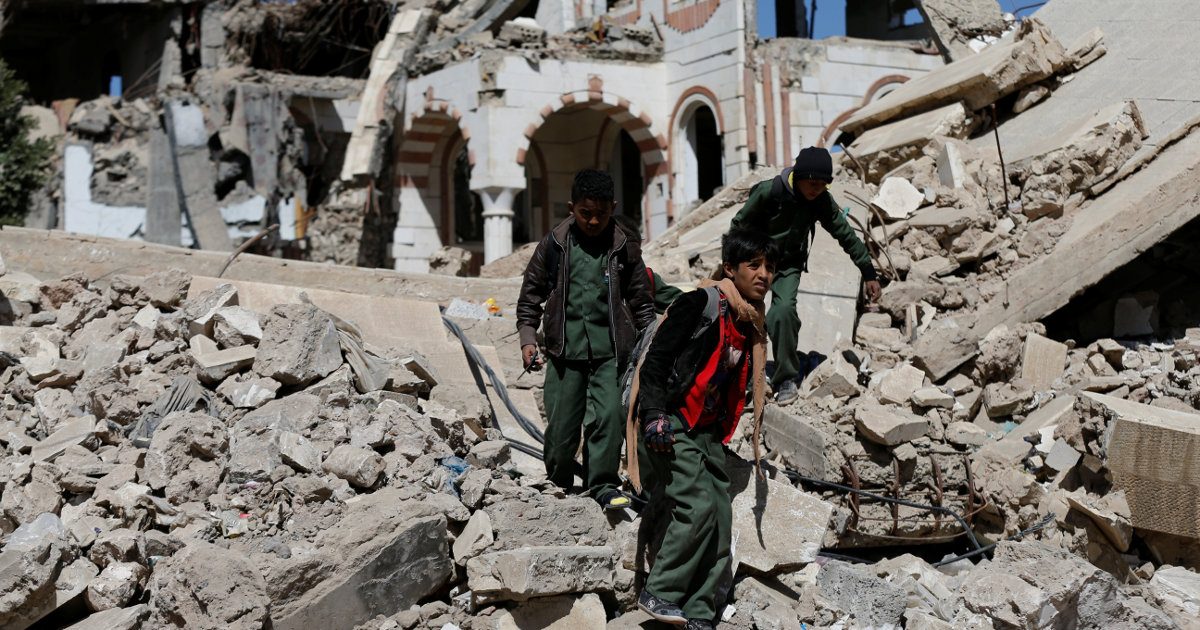 Unos niños caminan sobre unos escombros de edificios bombardeados en Yemen