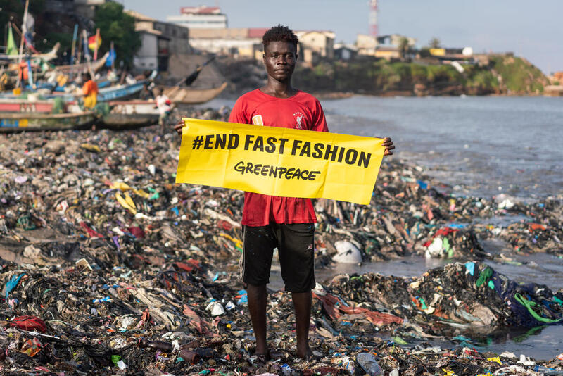 una persona local de Jamestown en Accra sujeta un cartel de Greenpeace que pone End Fast Fashion